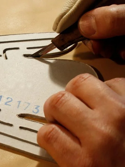 Leather being cut by hand using a shoemaking pattern for a pair of creepers